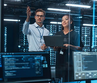 Female e-Business Entrepreneur and Male IT Specialist Discussing Something and Use Laptop in Big Data Center Server Room. Work on Web Services Cloud Computing SAAS Concept