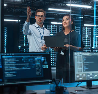 Female e-Business Entrepreneur and Male IT Specialist Discussing Something and Use Laptop in Big Data Center Server Room. Work on Web Services Cloud Computing SAAS Concept